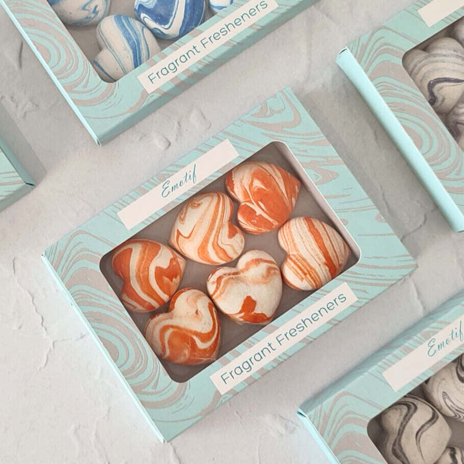 Marble-patterned scented candles in decorative boxes on a light gray surface