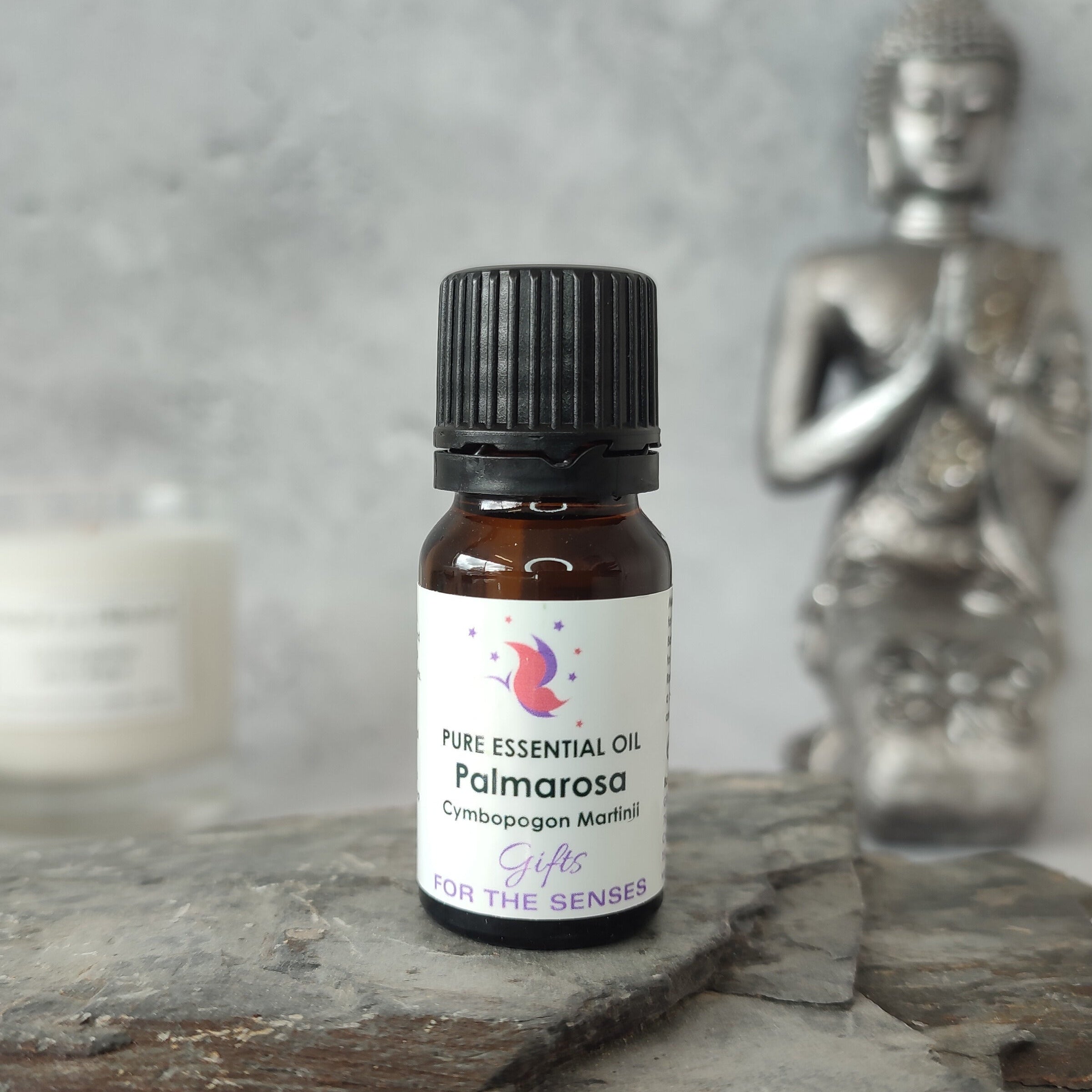 Bottle of Palmarosa essential oil on a wooden surface with a Buddha statue in the background.