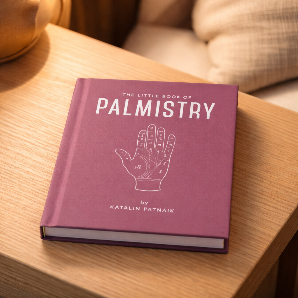 Purple book titled 'The Little Book of Palmistry' by Katalin Patnaik on a wooden surface.