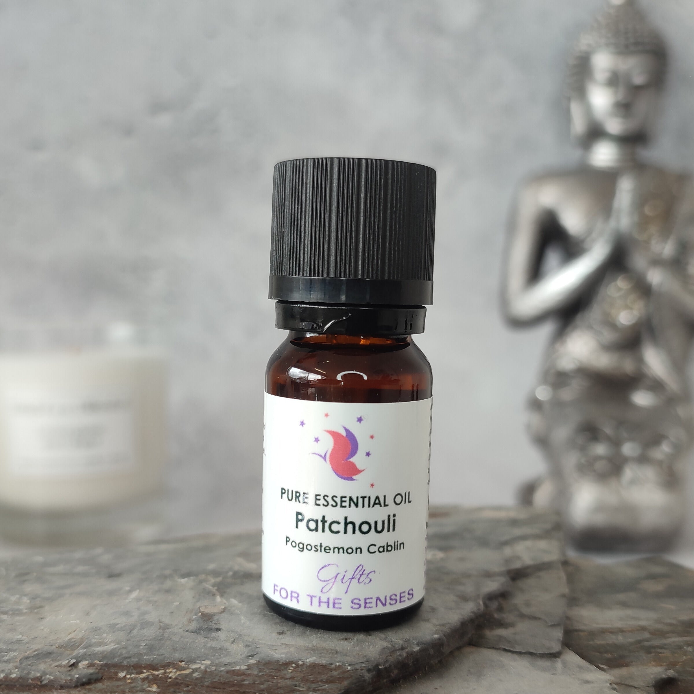 Patchouli essential oil bottle on a stone surface with a Buddha statue in the background