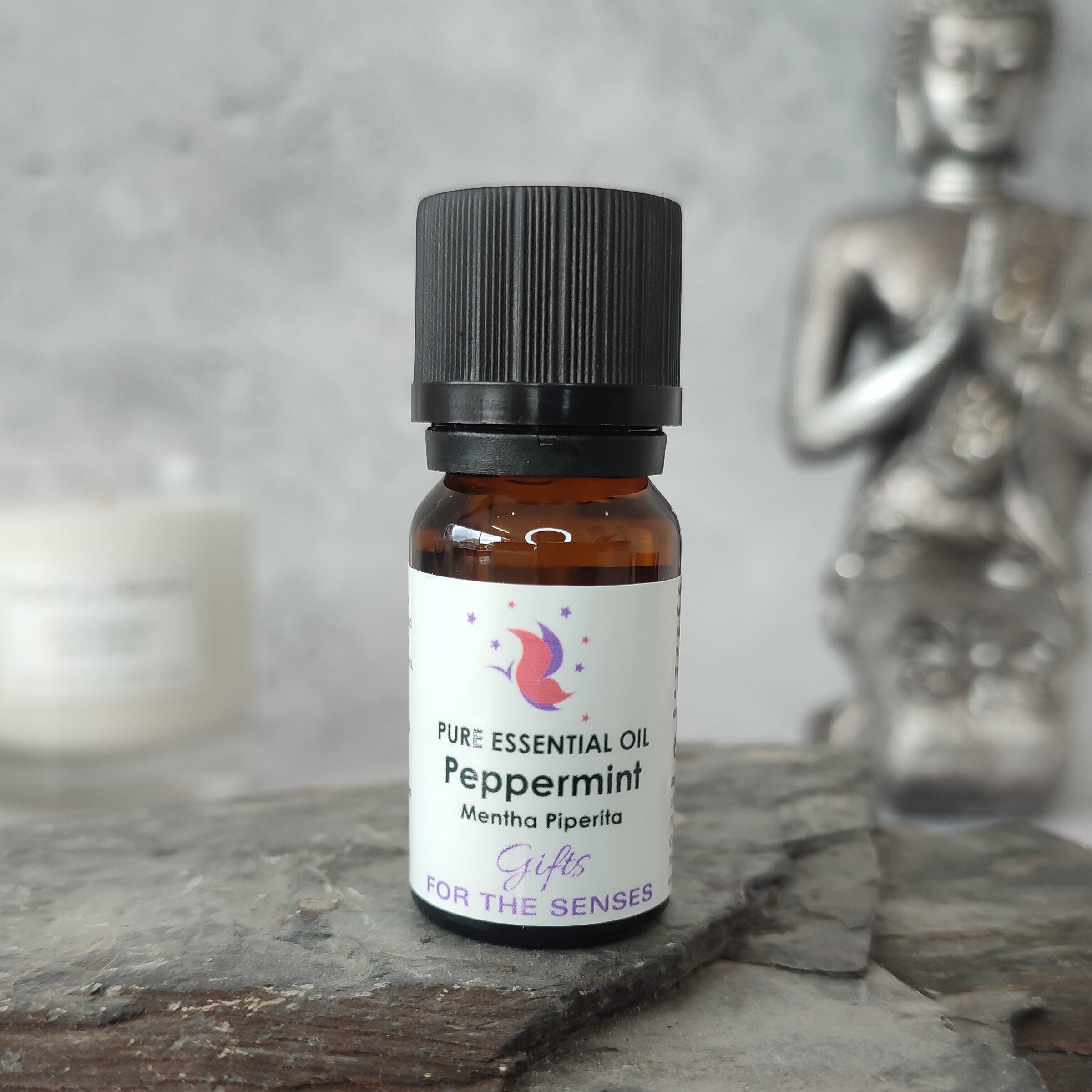 Peppermint essential oil bottle on a stone surface with a Buddha statue in the background