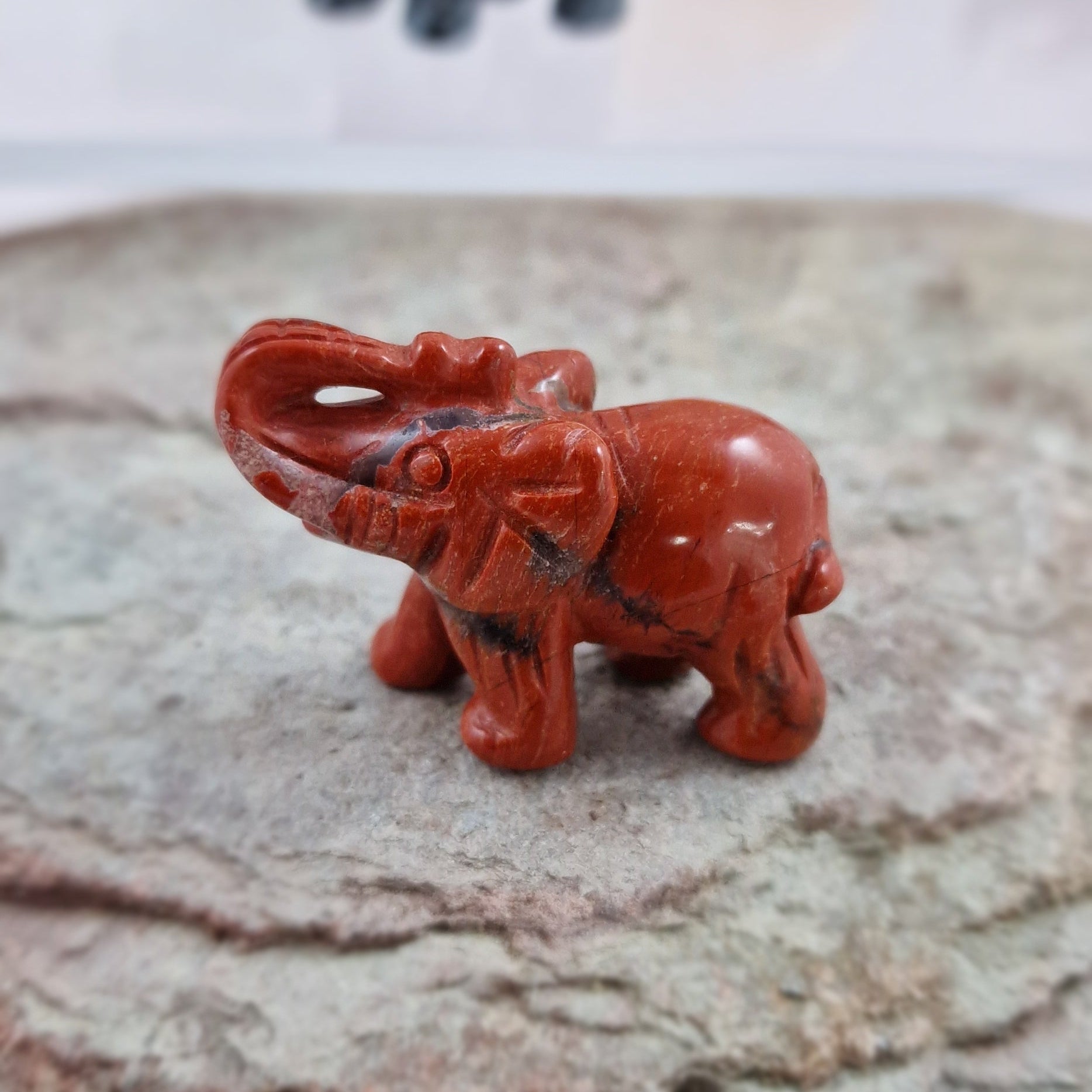 Red Jasper elephant on a rock with other crystal elephants in the background