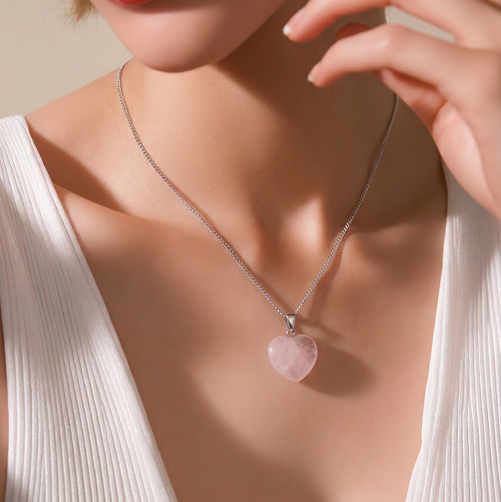 Necklace with a heart-shaped pink pendant worn by a model in a white top.