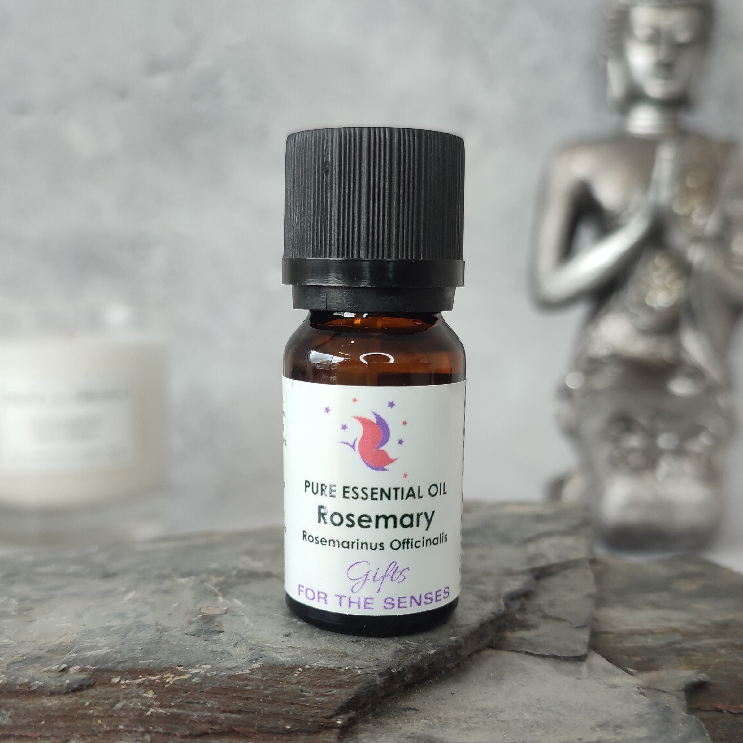 Bottle of rosemary essential oil on a stone surface with a candle and statue in the background