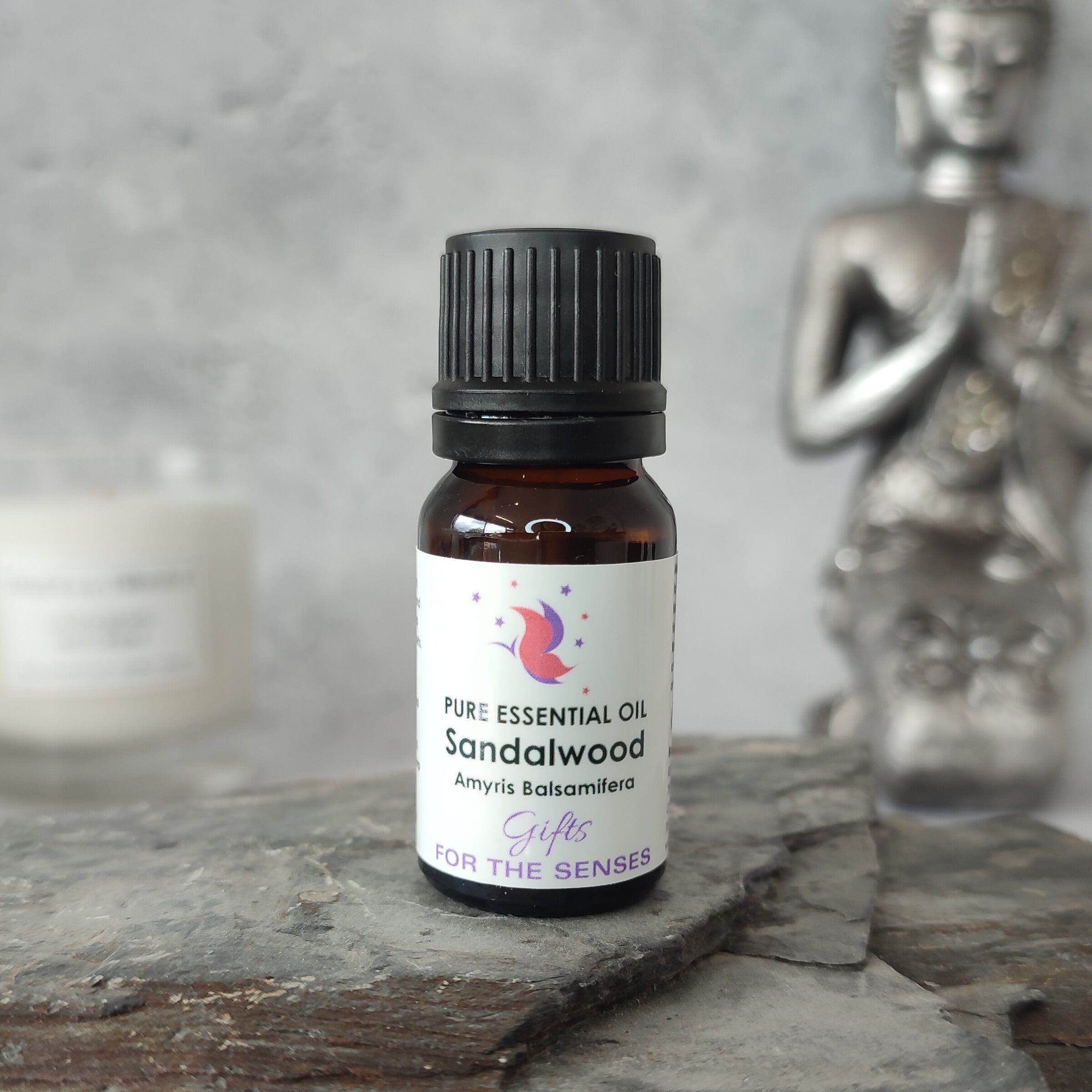 Sandalwood essential oil bottle on a wooden surface with a Buddha statue in the background