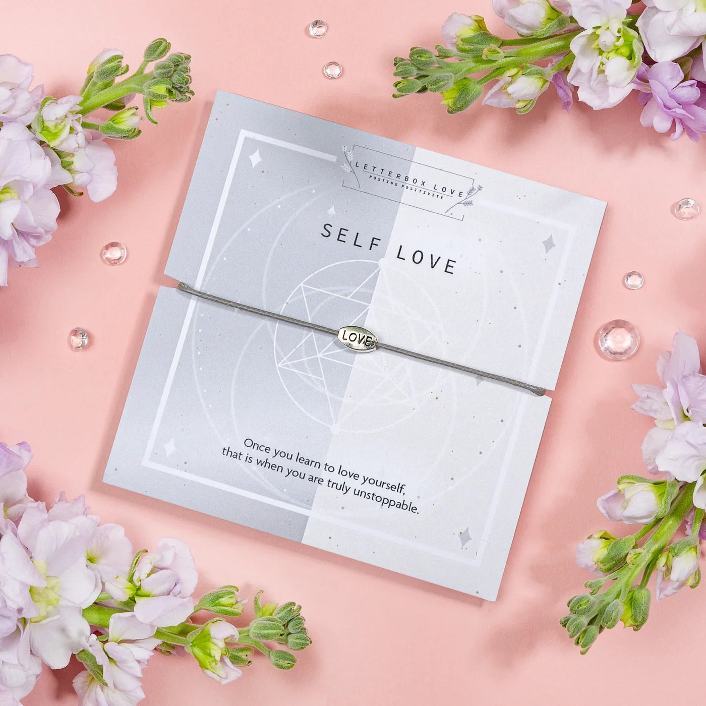 Silver bracelet with 'Self Love' message card on a pink background with flowers