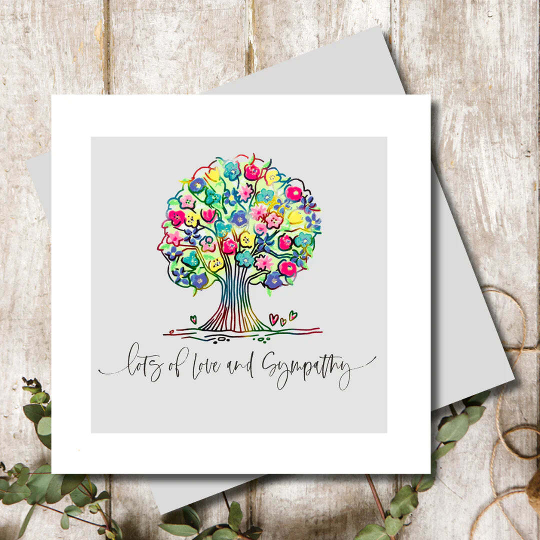 Greeting card with a colorful tree design and 'lots of love and sympathy' text on a wooden surface.