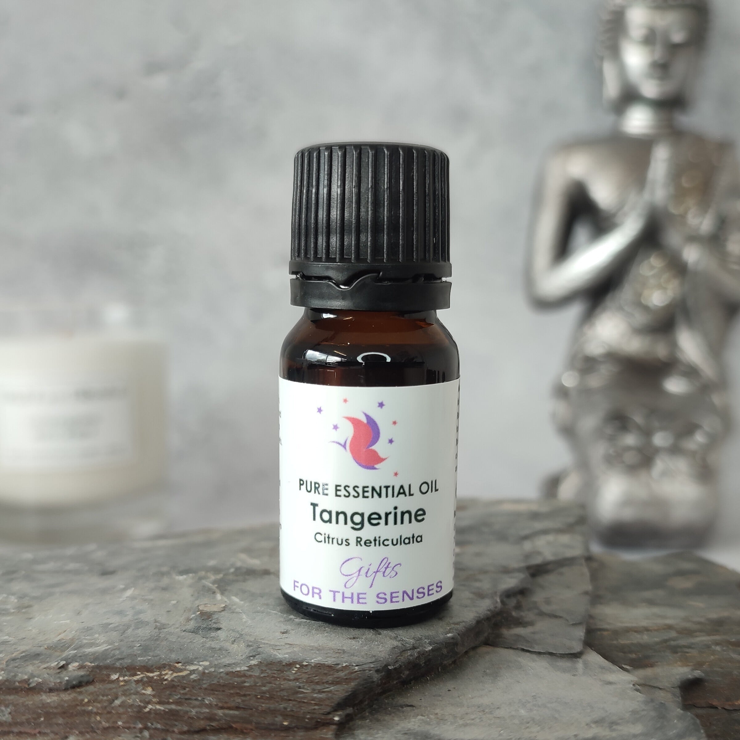 Bottle of tangerine essential oil on a slate surface with a Buddha statue in the background