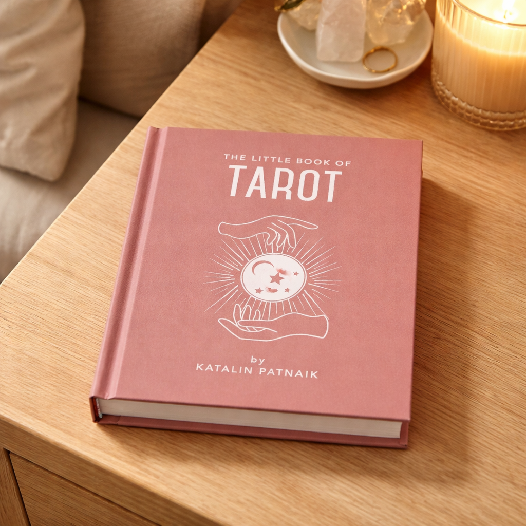 Pink book titled 'The Little Book of Tarot' by Katalin Patnaik on a wooden table.