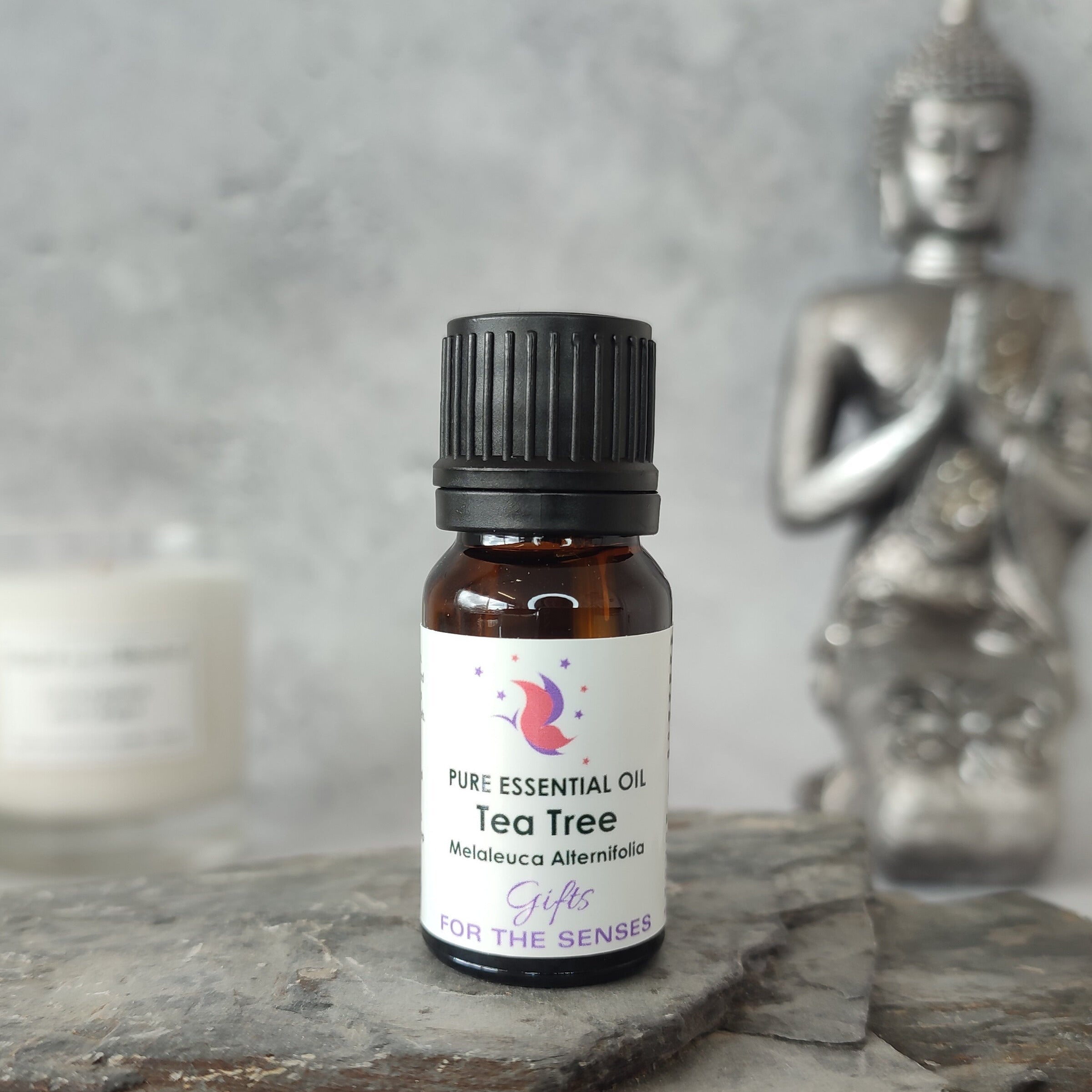Tea tree essential oil bottle on a slate surface with a Buddha statue in the background