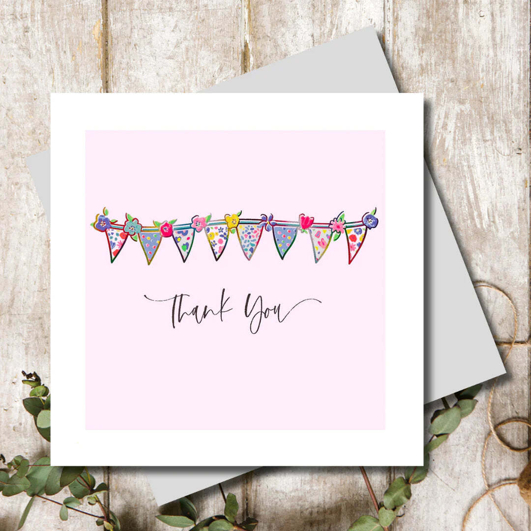 Greeting card with colorful bunting design and 'Thank You' text on a pink background, placed on a wooden surface.