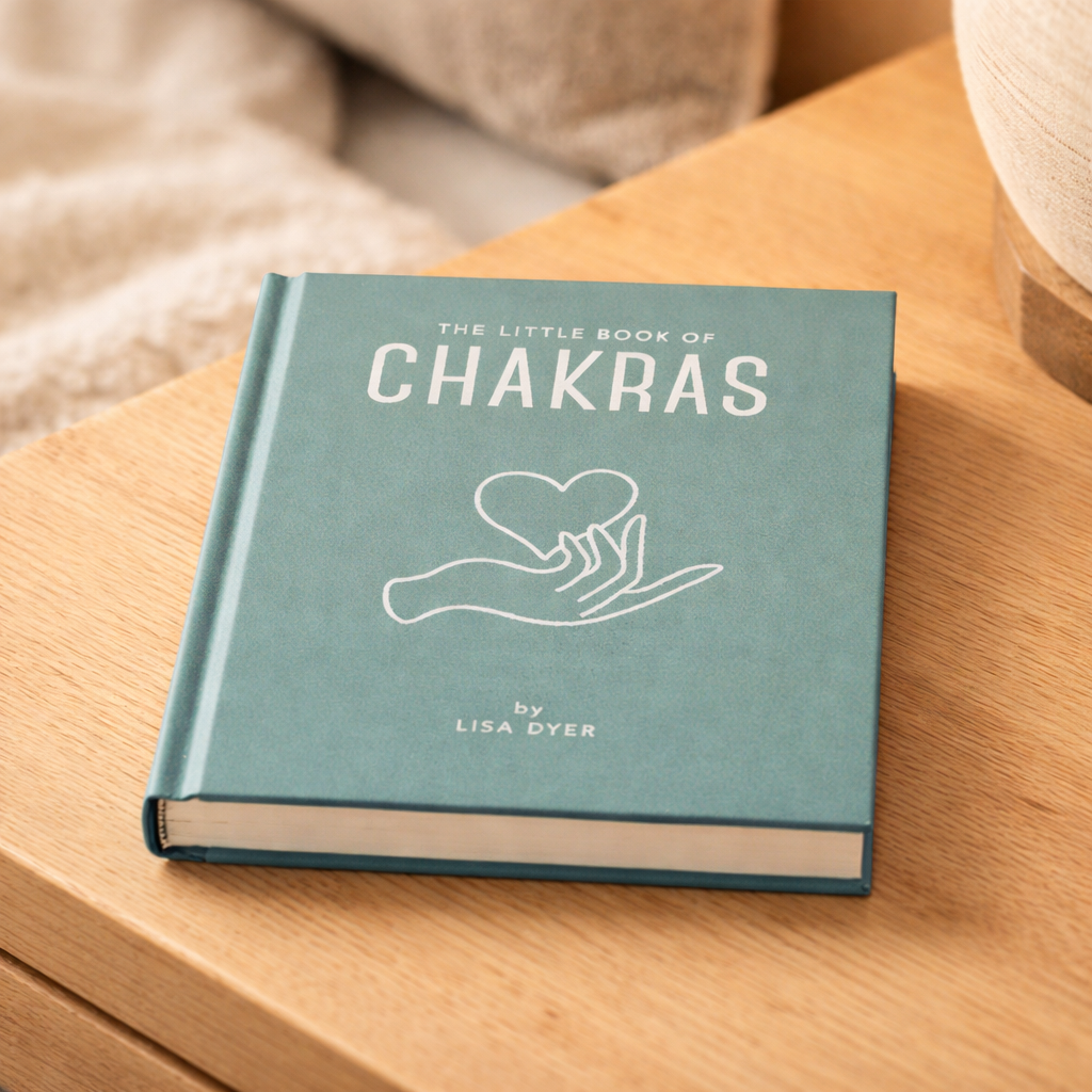 Blue book titled 'The Little Book of Chakras' by Lisa Dyer on a wooden surface.