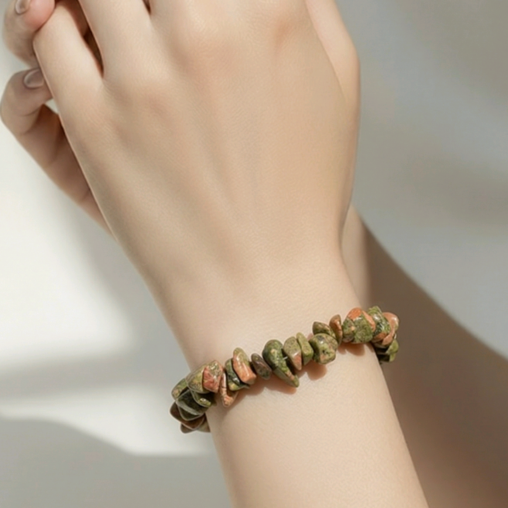 Hand wearing a Unakite chip bracelet on a neutral background