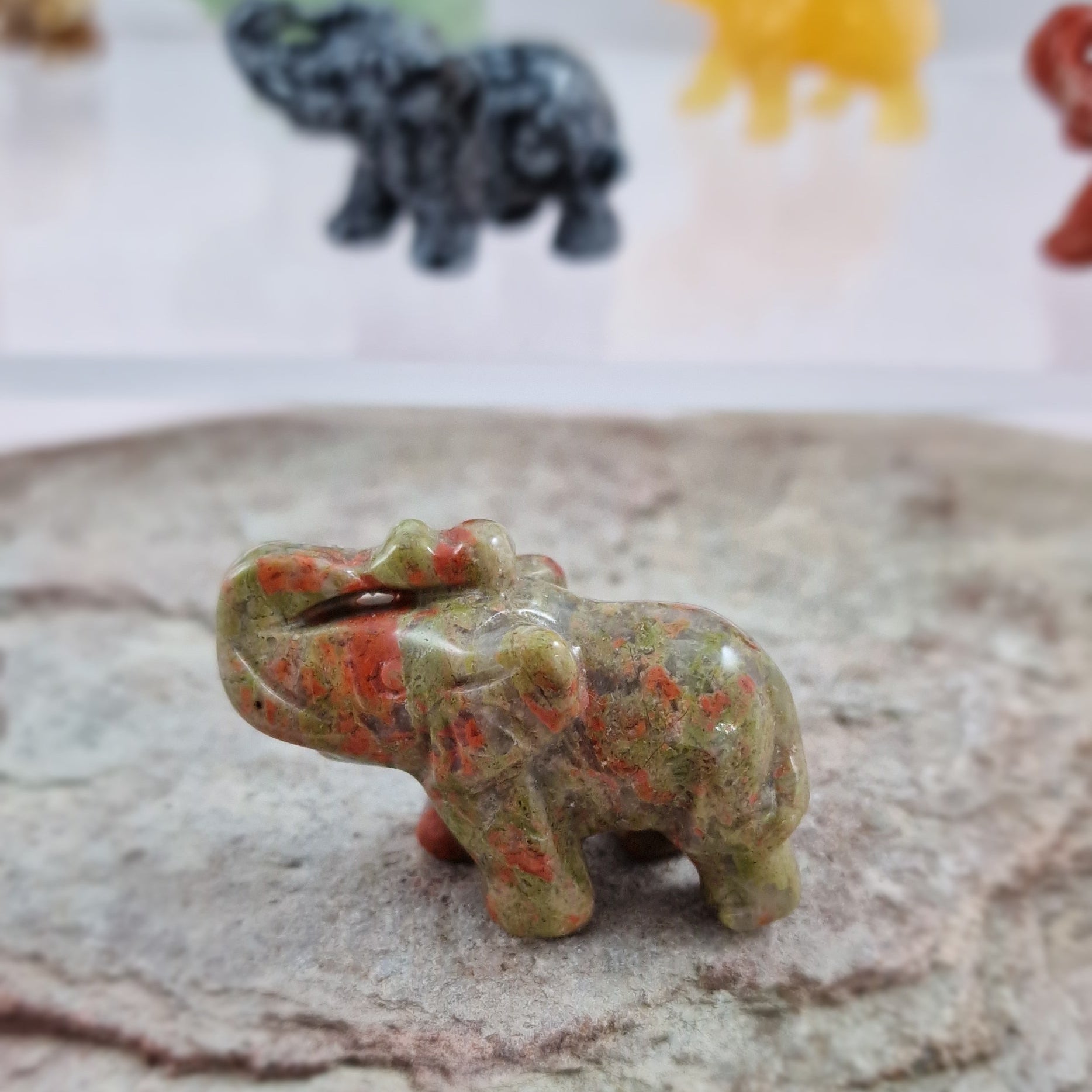 Small unakite crystal  elephant carving on a textured surface with colorful stones in the background